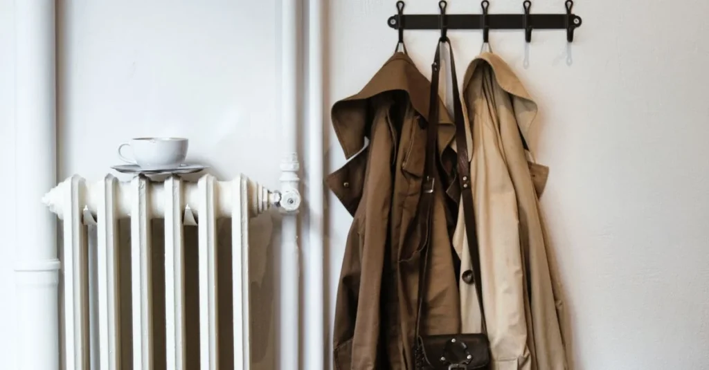 Folded overcoat and sweater on a brass clothing rack in soft window light