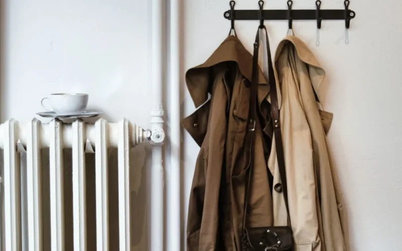 Folded overcoat and sweater on a brass clothing rack in soft window light