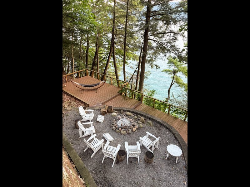 Fire pit and white chairs on lower deck overlooking a calm lake at dusk