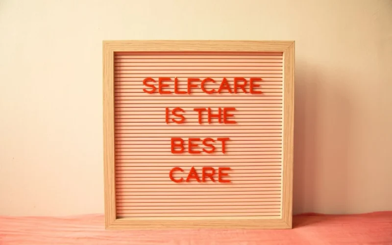 Wooden letter board reading self care is the best care in orange letters