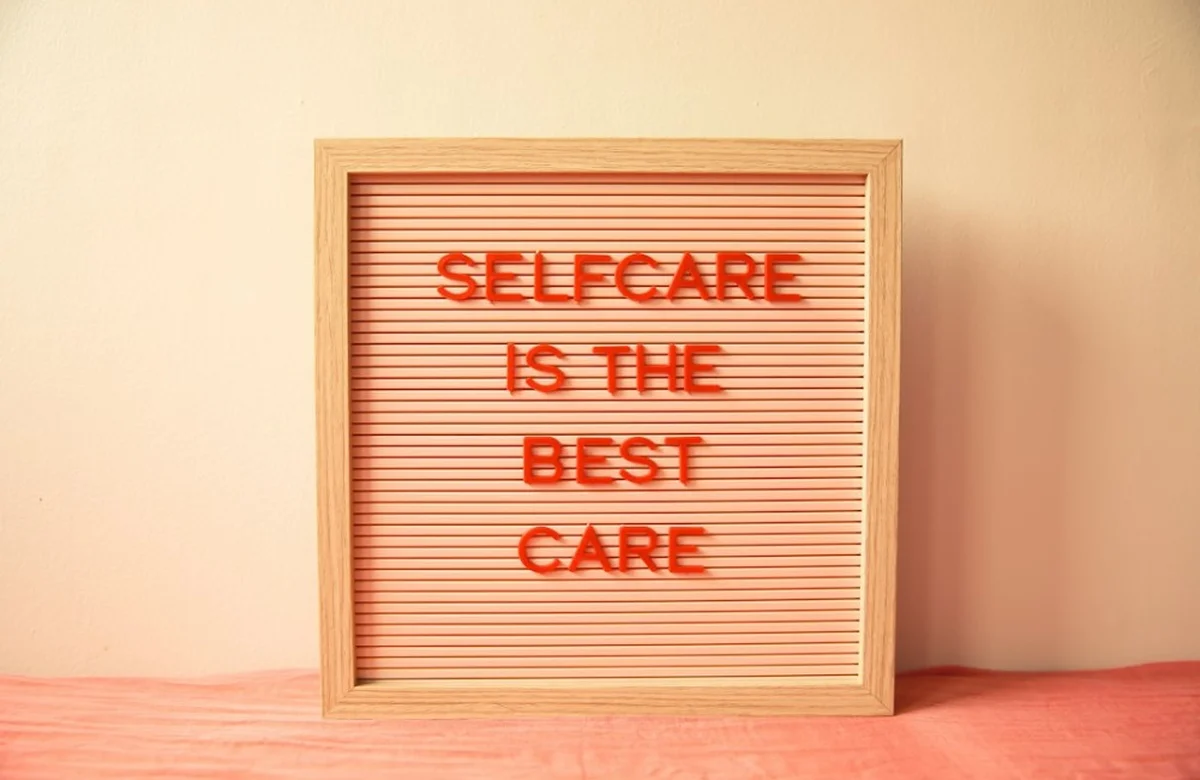 Wooden letter board reading self care is the best care in orange letters