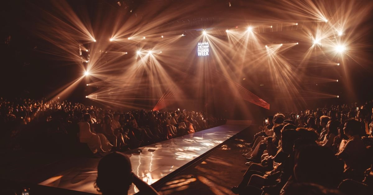 Wide view of a fashion show runway with bright spotlights and seated audience